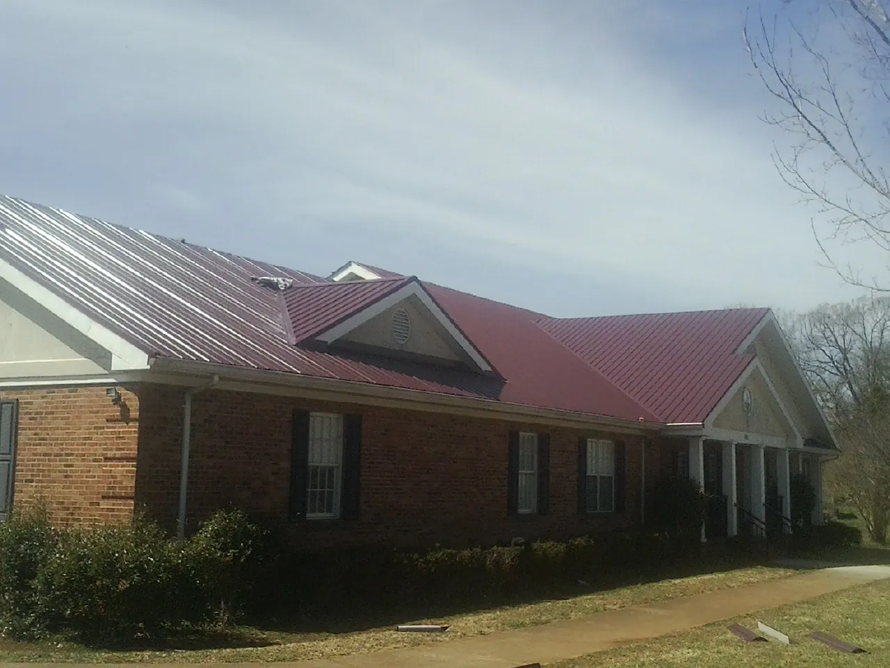 Red metal roof with gabled entries on a long brick building, from a Hail Damage Roof Repair job in Lock Haven