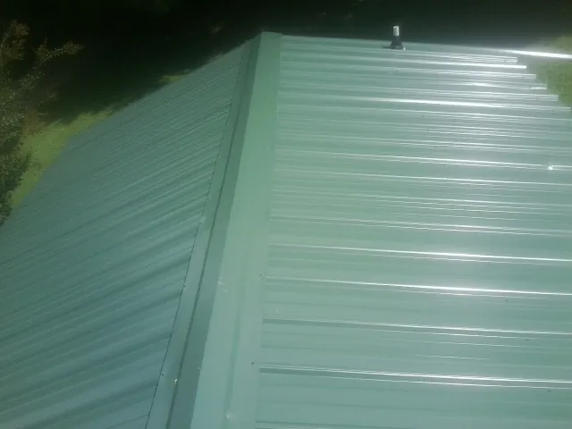 New green metal panels meeting at the ridge of a roof — Flat Roof Repair work by our crew in Lock Haven