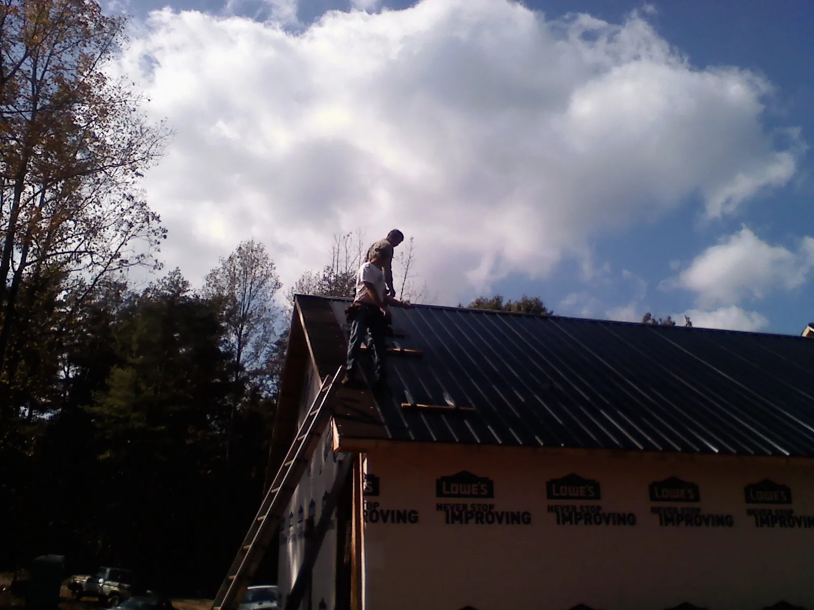 Roofer fastening dark metal panels high against a cloudy sky, from a Roof Inspection job in Lock Haven