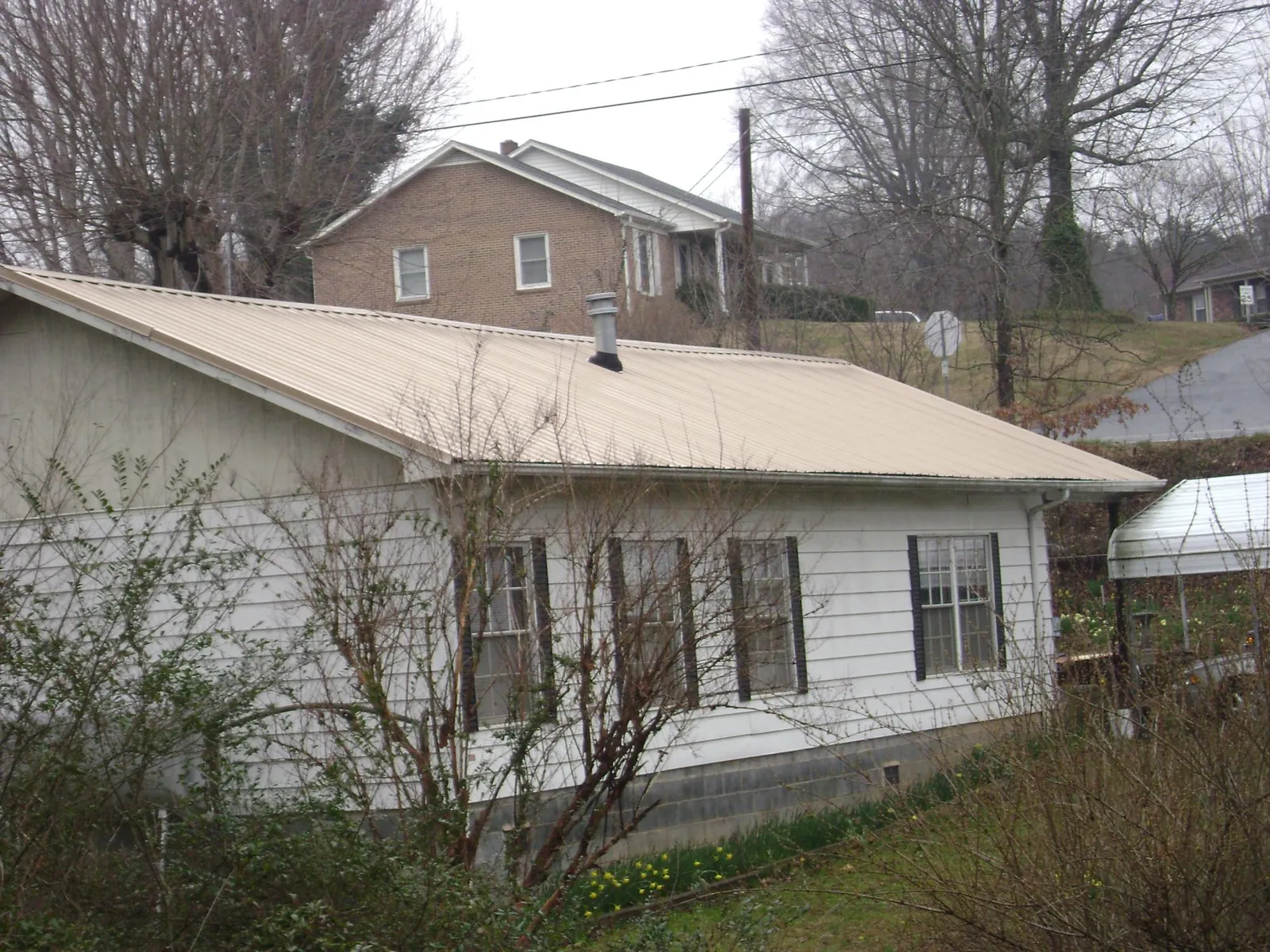 Tan metal roof on a white sided house set into a hillside — Commercial Roofing by Roofing Brothers in Lock Haven